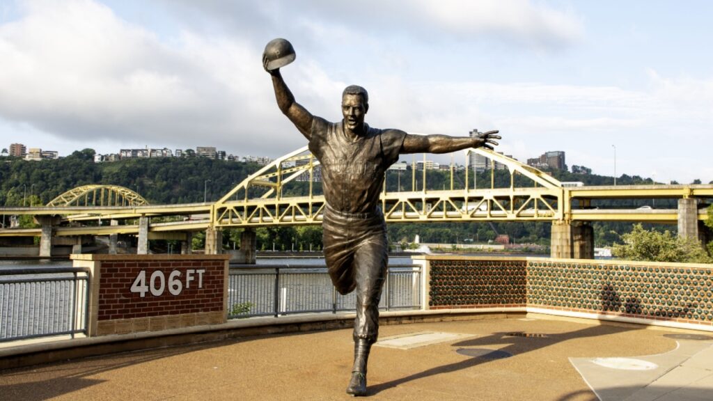 Front view of the Bill Mazeroski Statue at PNC Field in the city of Pittsburgh Pennsylvania with yellow and gold bridges in the background.