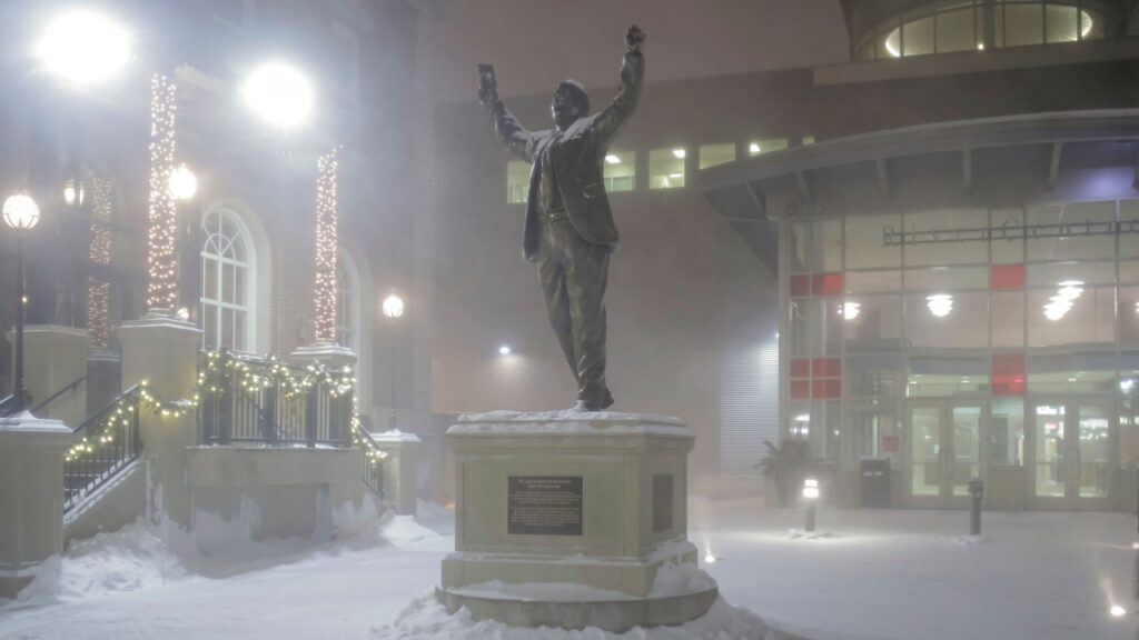 A statue of Herb Brooks of NHL Fame in Downtown St. Paul on a snowy winter night.