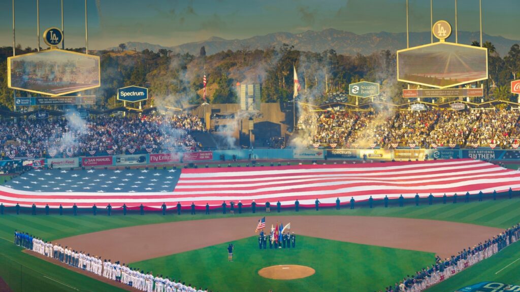 The USA flag spread out in a baseball stadium with a packed crowd.