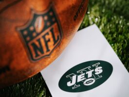 New York Jets logo on the ground and official NFL ball on green grass.