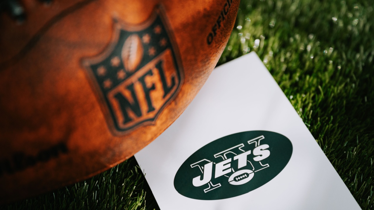 New York Jets logo on the ground and official NFL ball on green grass.