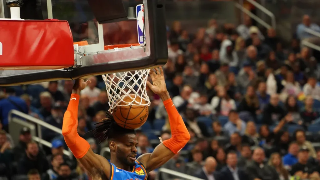 A basketball player in an orange uniform dunks the ball during a game.