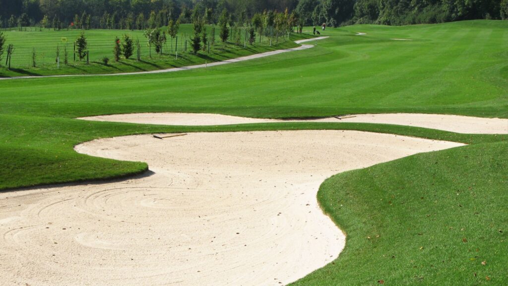 Large sand bunker guarding elevated green on challenging golf course hole.