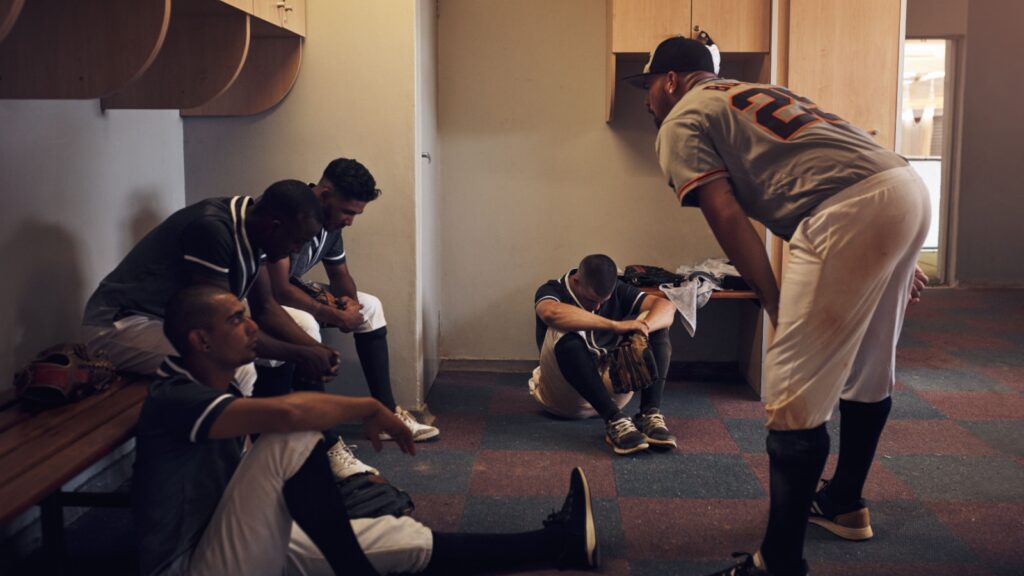 Dejected baseball players sitting in locker room.