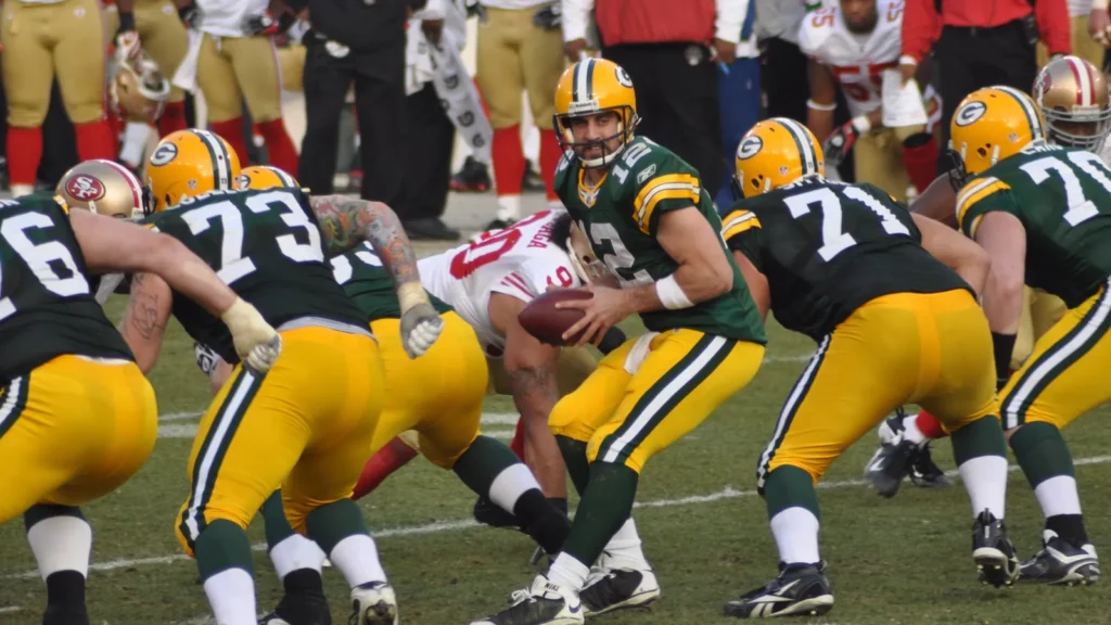 An American football quarterback prepares a handoff while linemen block during a play.
