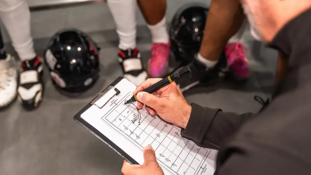 American football coach holding a clipboard drawing strategies.