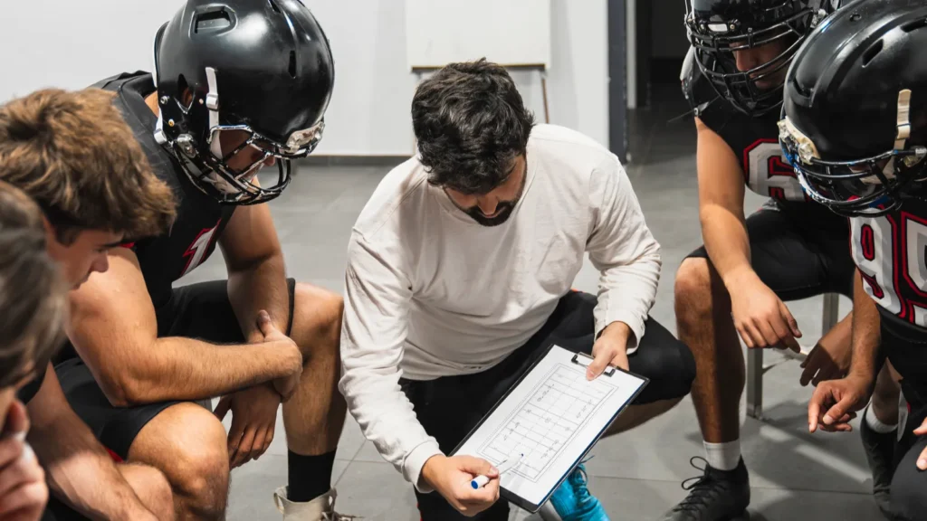 An American football coach showing strategy on a clipboard to his players.