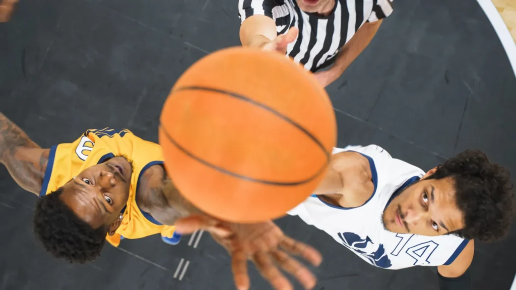 Overhead view of basketball tip-off with two players competing for the ball.