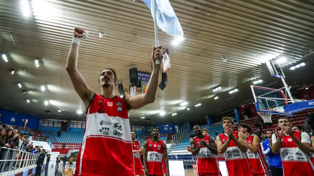 Basketball player celebrating championship victory with arms raised in arena with crowd.