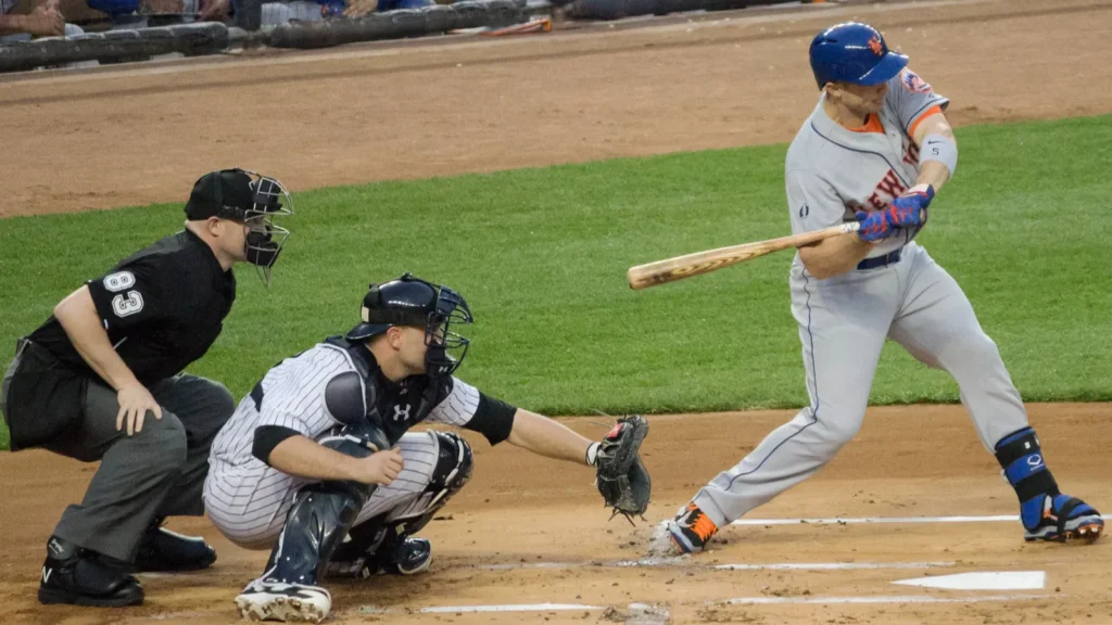 MLB umpire behind catcher watching batter swing during live game action.