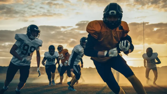 two professional american football teams stand opposite each other ready American football players in full gear running a play during sunset practice on a dusty field.