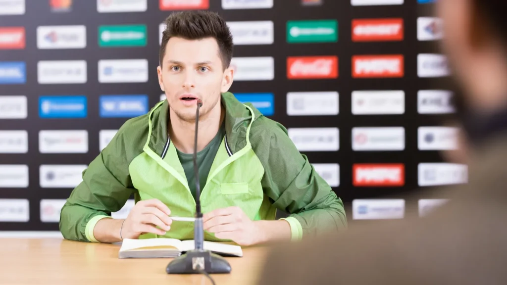 Sports coach addressing the media at the official press conference table.