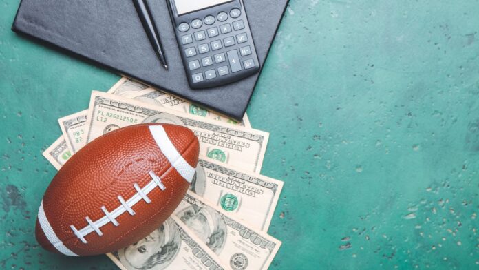 Football with dollar bills and a calculator kept on the green surface.