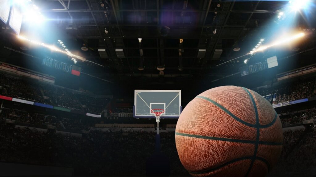 Basketball ball on the floor in a basketball arena with hoop and floodlights.