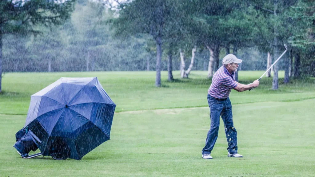 A golfer on a rainy day swinging in the fairway.