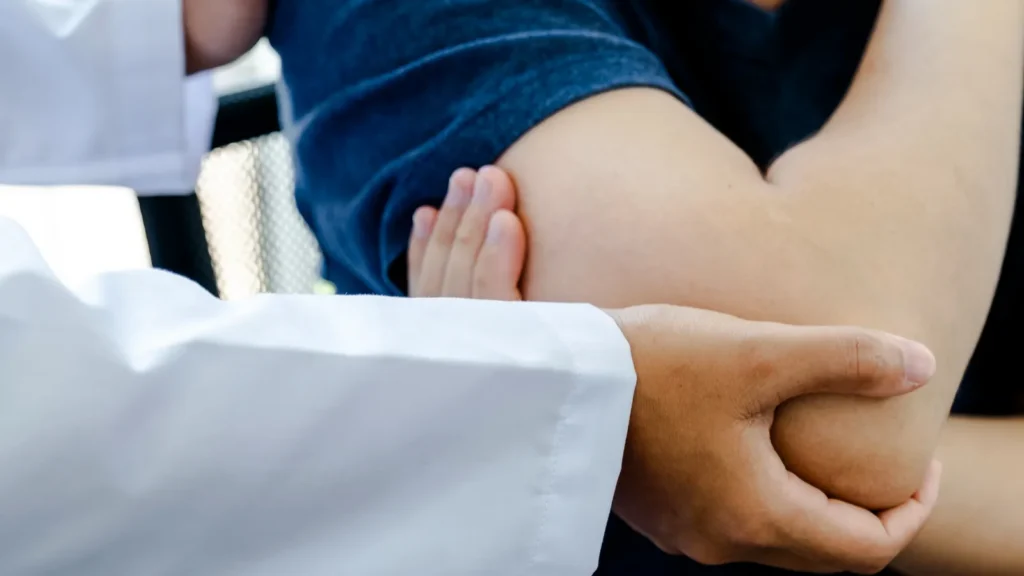A doctor examining a patient's shoulder and elbow during a medical consultation.