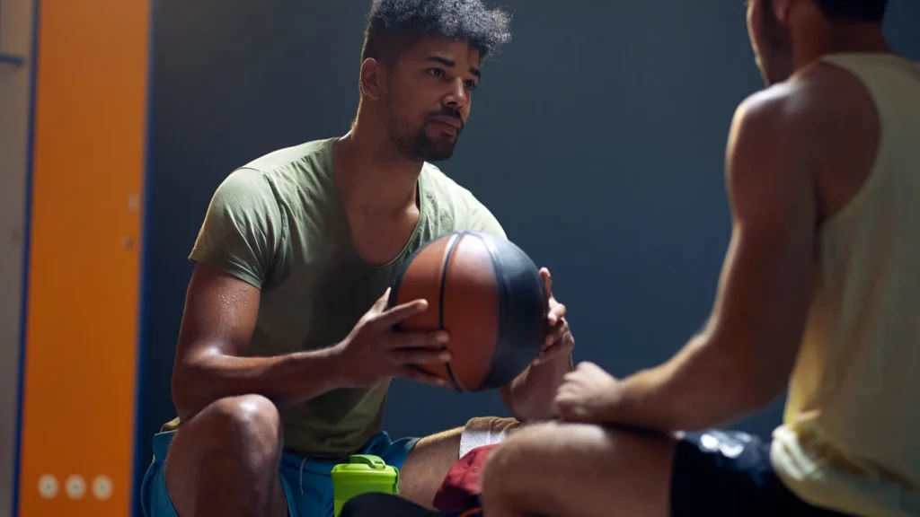 Two basketball players sitting in the dressing room.