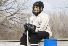 The untold story behind the NHL’s emergency backup goalies An ice hockey player holding a hockey stick sitting on the sideline.