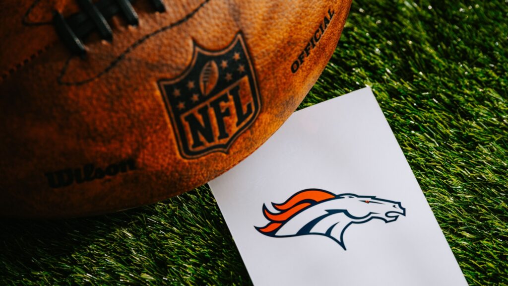 Denver Broncos NFL team logo and American football ball on green grass.