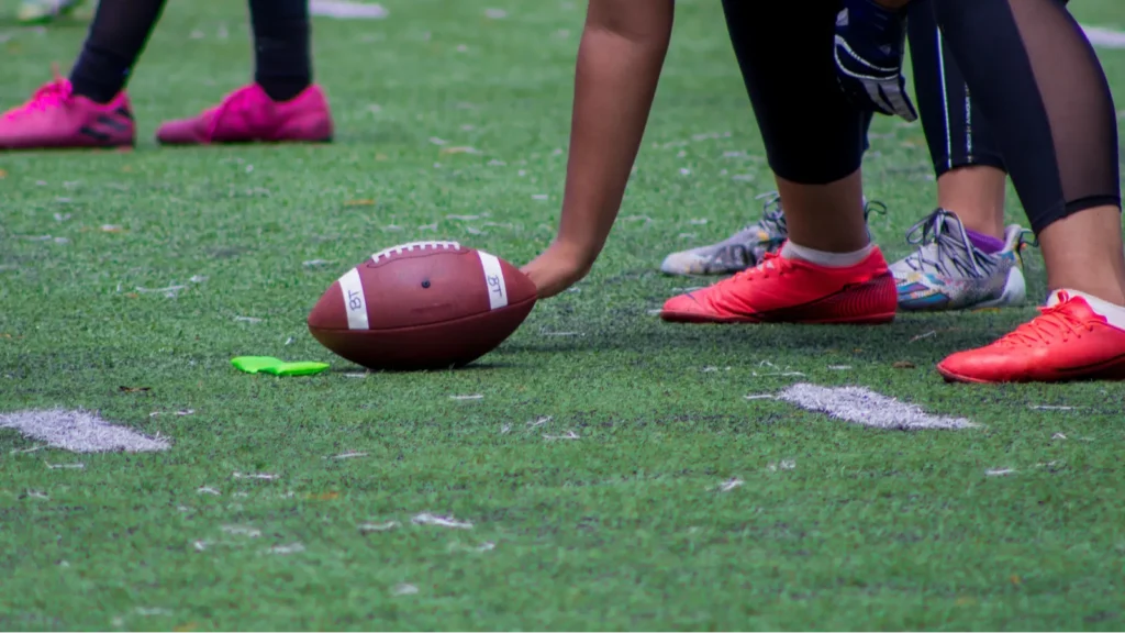 A closeup shot of an American football ball between players hands during a match on a green field