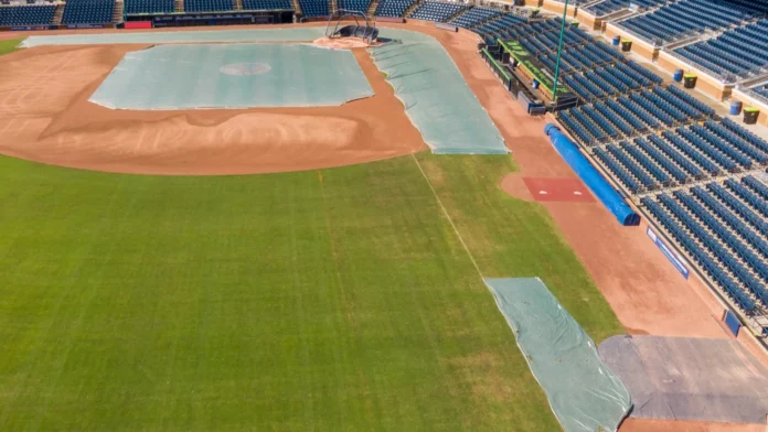 Aerial drone view overlooking the third base side of Durham Bulls Athletic Park The shot shows the green outfield grass transitioning to the dirt infield which is partially protected by large green tarps near the bases and pitchers mound