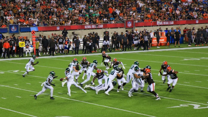 An American football game between the Cleveland Browns and the Jets in progress at a packed stadium at night. An American football game between the Cleveland Browns and the Jets in progress at a packed stadium at night.