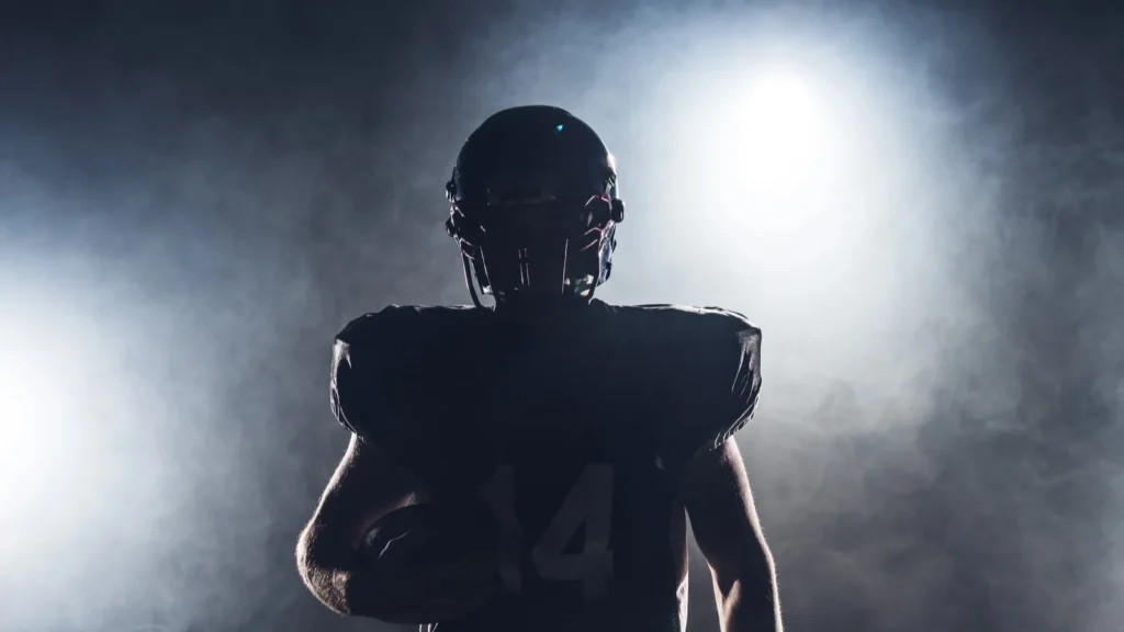 Dark silhouette of an equipped American football player with ball against white smoke.