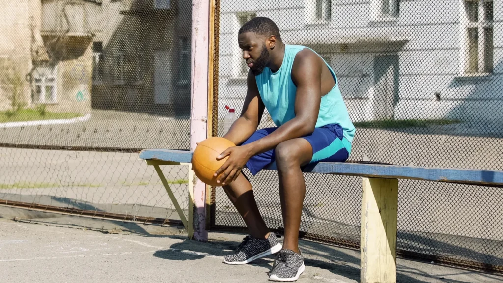 A lonely basketball player sitting on the bench and holding a ball.