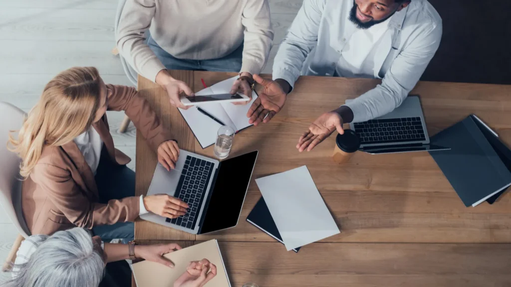 overhead view of multicultural colleagues talking and sitting at table during meeting