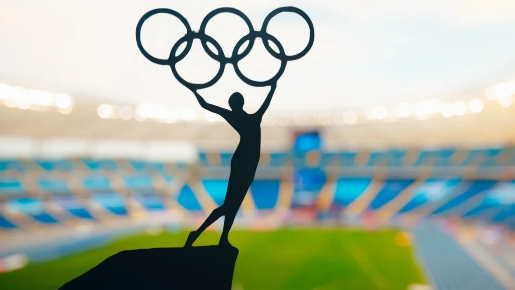 A silhouette holding the Olympic rings above a packed stadium.