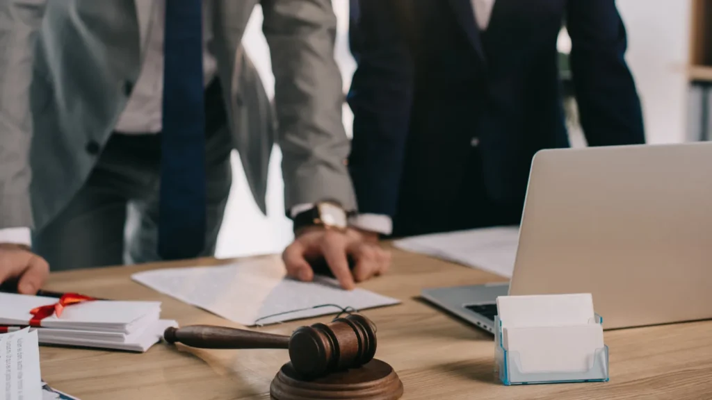 partial view of lawyers in suits working together on project at workplace with gavel and laptop in office