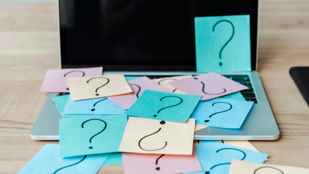 Selective focus of sticky notes with question marks on laptop with blank screen near notebook