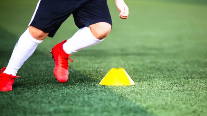 Selective focus to cone marker with blurry boy soccer player is jogging on green artificial turf Material for training class of football academy