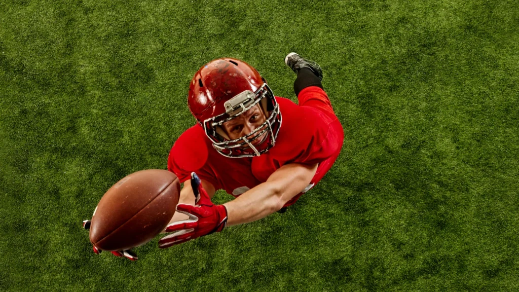Top view image of concentrated man American football player in red uniform in motion on stadium catching ball with precision Concept of sport competition tournament game Copy space