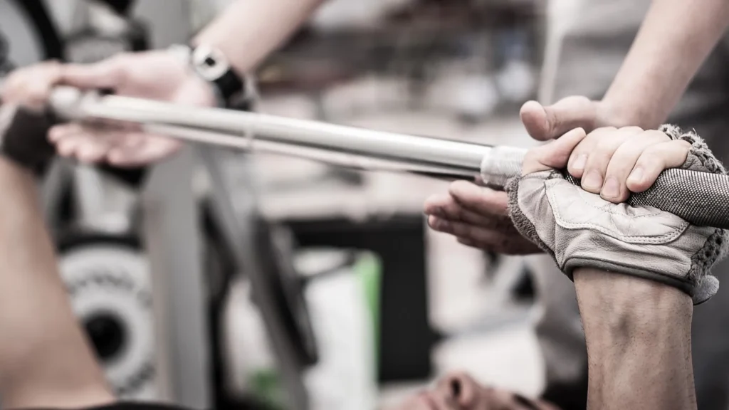 Young man lifting the barbell in the gym with instructor Focus on hand