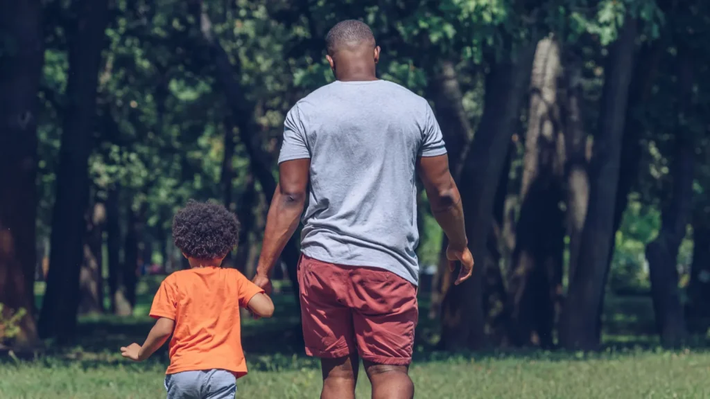 back view of african american father and son holding hands while walking in park