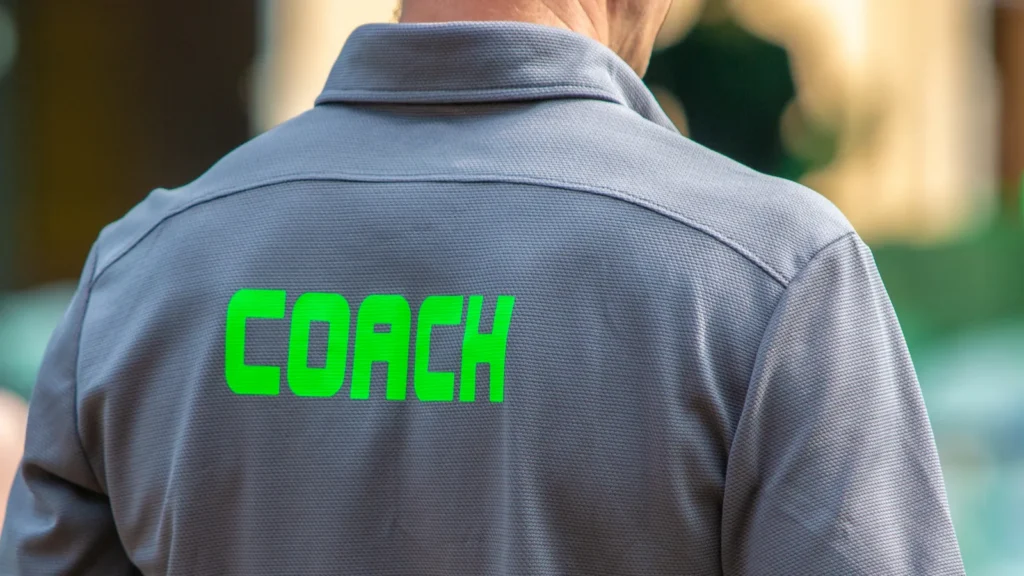 Back view of a male coach wearing COACH shirt outdoors.