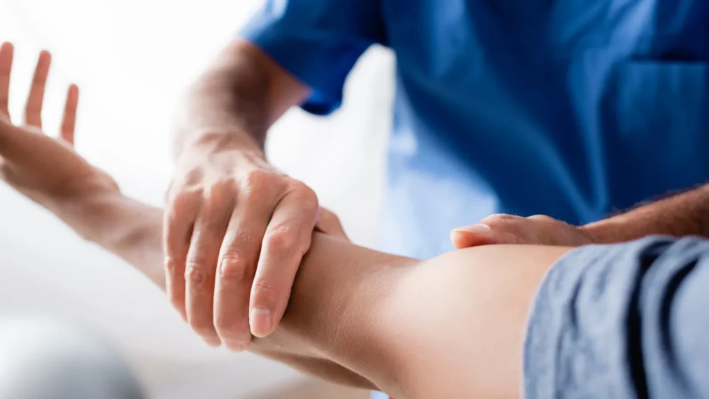 cropped view of chiropractor working with injured arm of african american man in clinic