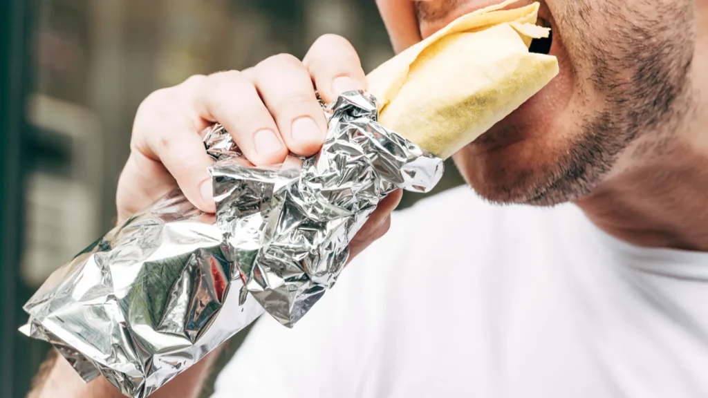 cropped view of man eating doner kebab in aluminium foil