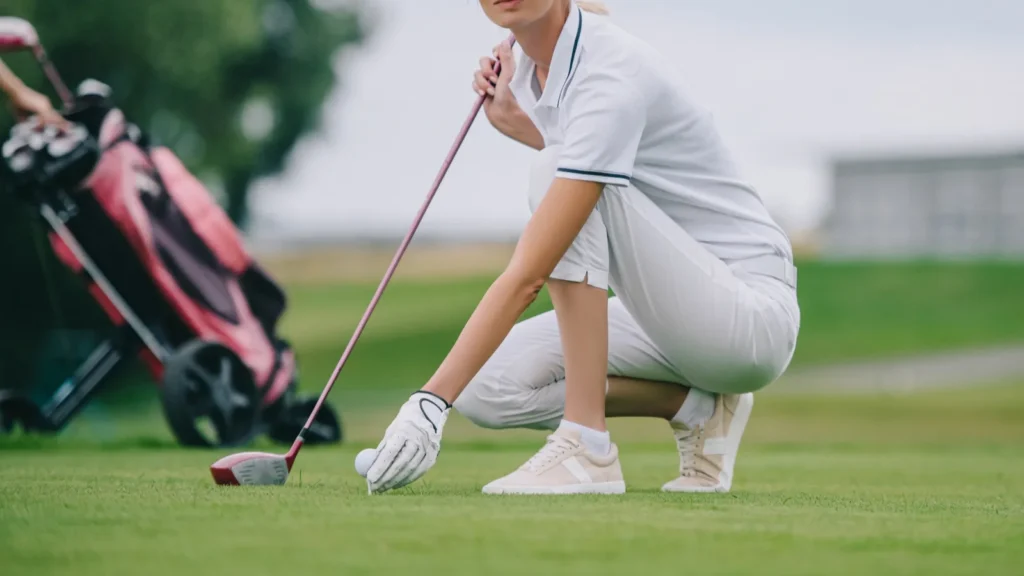 female golf player in cap and golf glove putting ball on green lawn at golf course