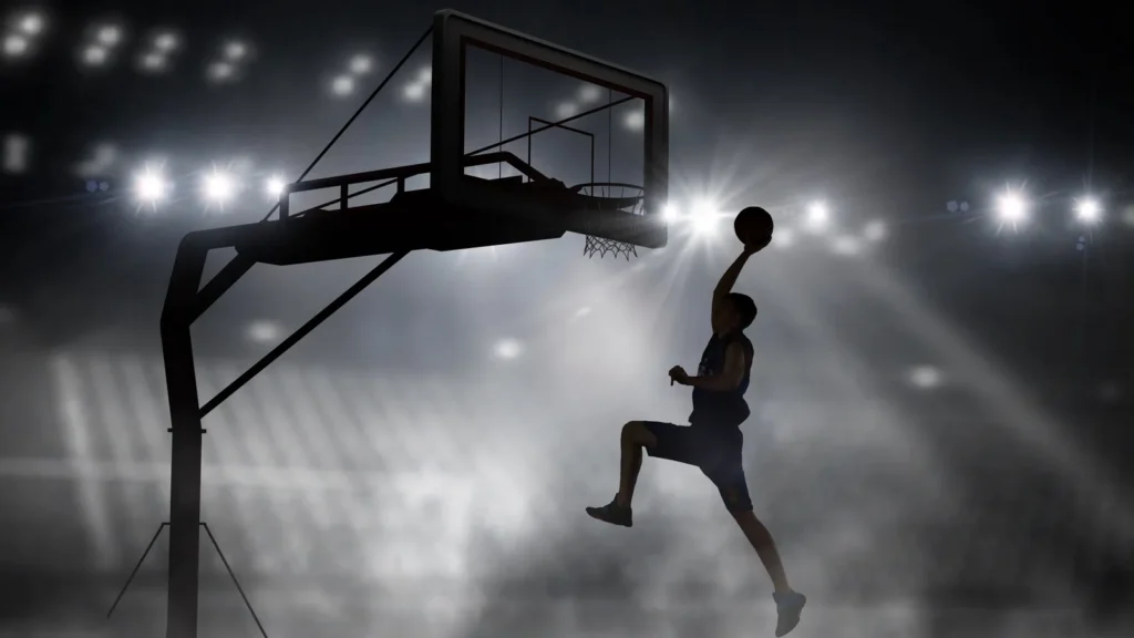 A basketball player's silhouette going up for a dunk under bright arena lights.