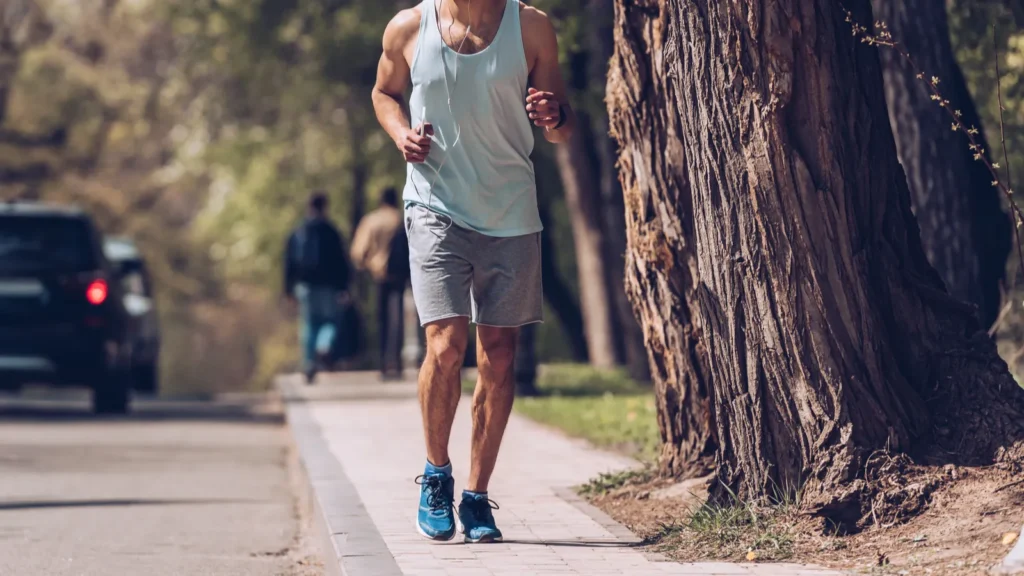 KYIV UKRAINE  APRIL 25 2019 Handsome sportsman running along pavement near roadway and listening music in earphones