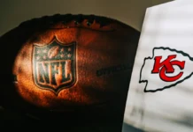NFL scout raises a red flag about Travis Kelce’s 2026 season An official NFL football alongside the logo of the Kansas City Chiefs team