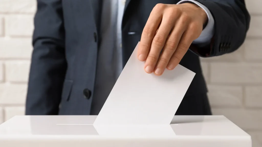 Man putting his vote into ballot box against brick wall closeup