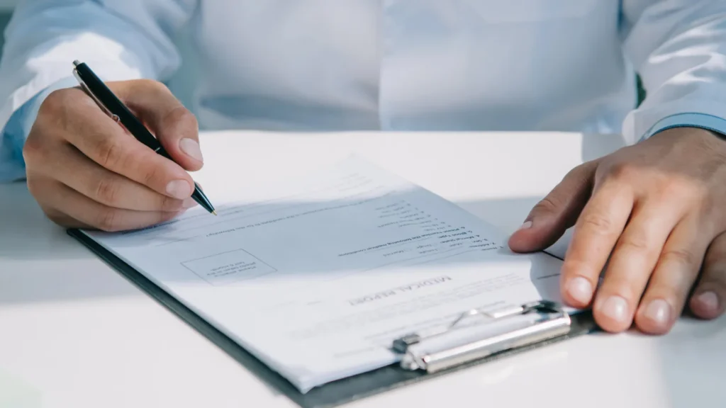 Partial view of doctor writing diagnosis in medical report on clipboard