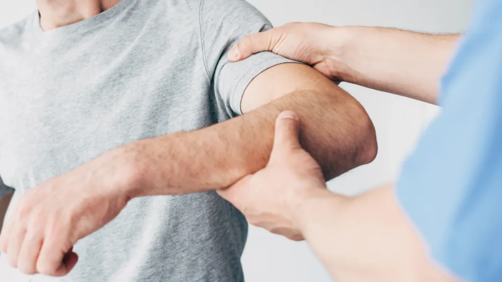 Selective focus of patient suffering from pain and doctor examining patient arm in massage cabinet at clinic