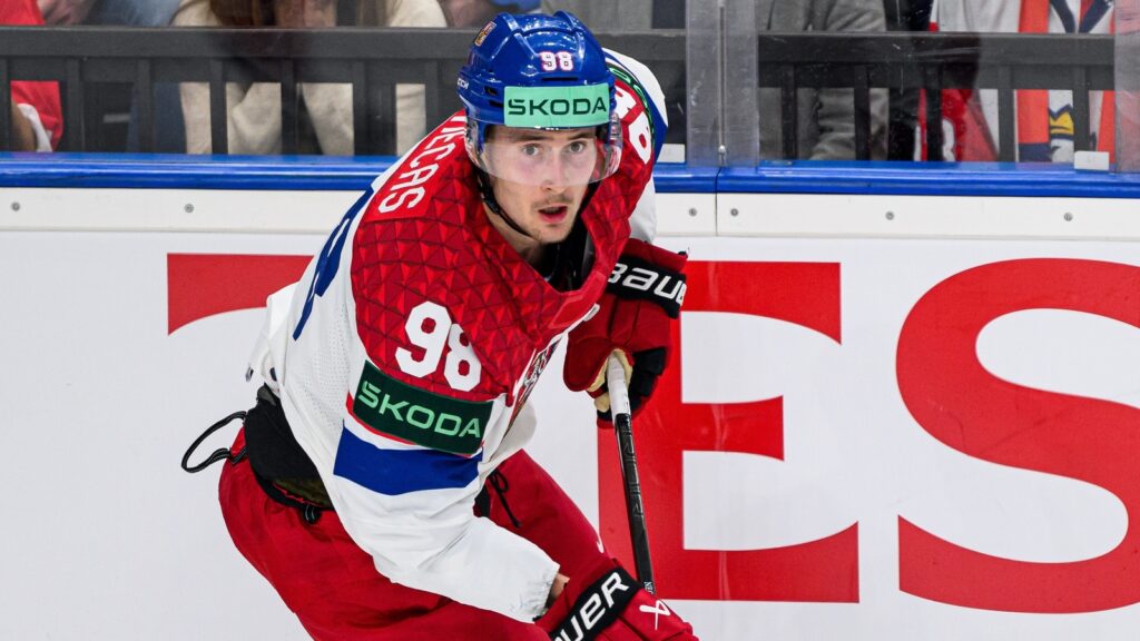 Ice hockey player in red-and-white jersey wearing number 98, skating with stick on the rink.