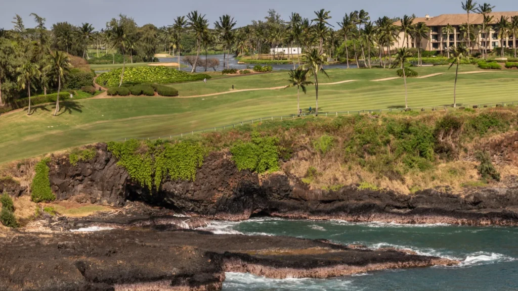 Golf course fairway overlooking rocky Pacific Ocean coastline in Hawaii.