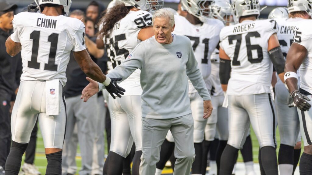 Las Vegas Raiders head coach Pete Carroll greets a player during team practice on the field.