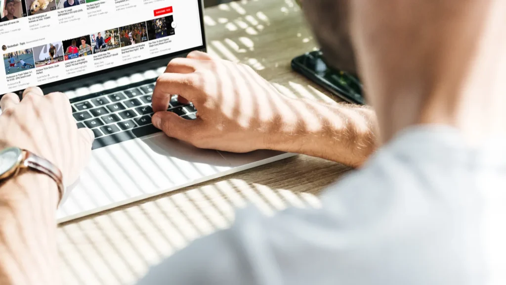 back view of man using laptop with youtube website on screen